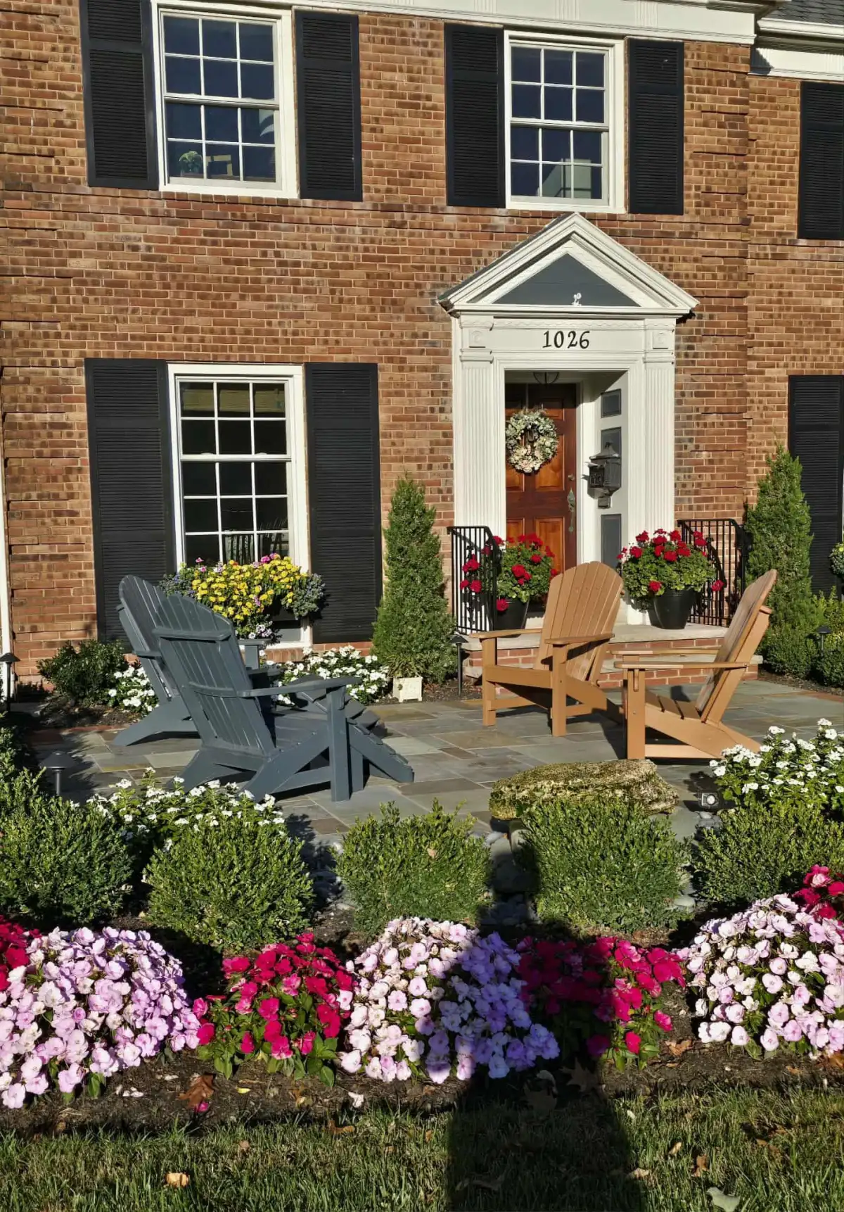 Brick home with colorful flower beds, Adirondack chairs, and professional landscaping