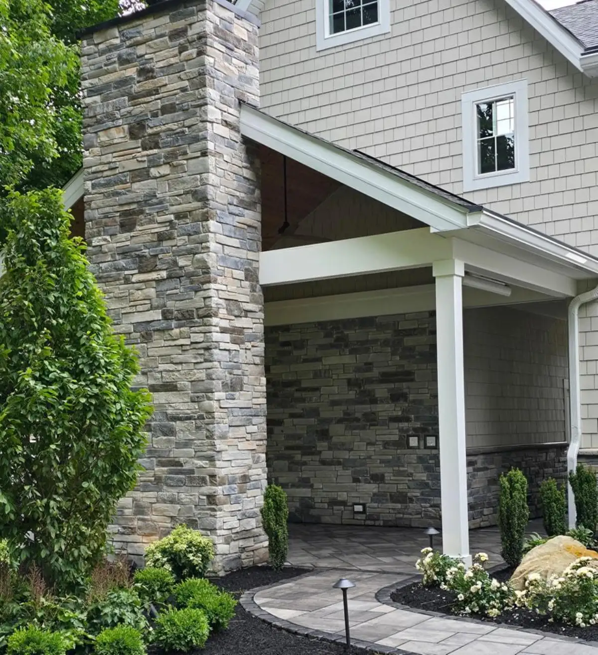 Stone-veneer columns with covered porch, curved paver walkway, and landscape lighting