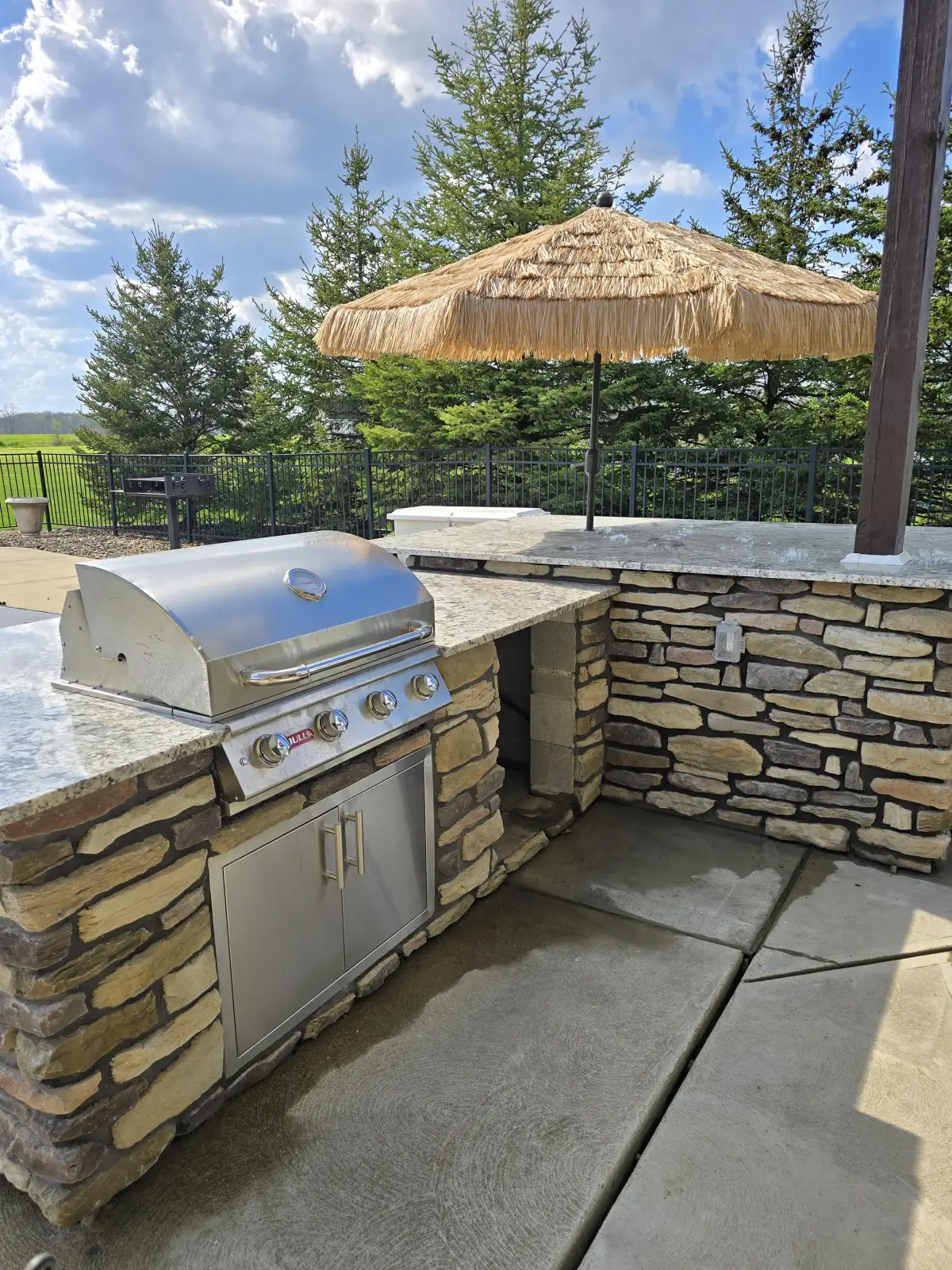 Stone outdoor kitchen with built-in Bull grill, granite countertop, and thatched umbrella