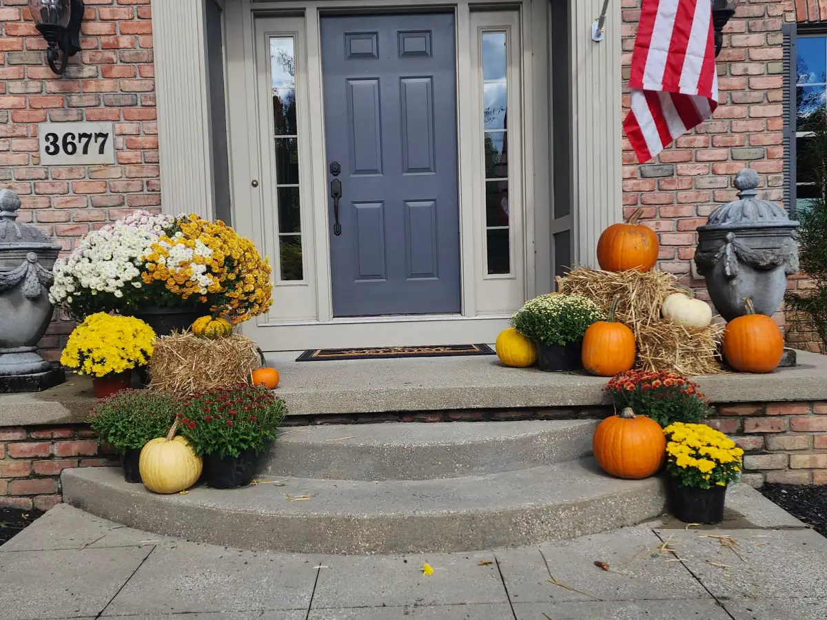 Brick home front entrance with American flag, seasonal mums, pumpkins, and decorative hay bales
