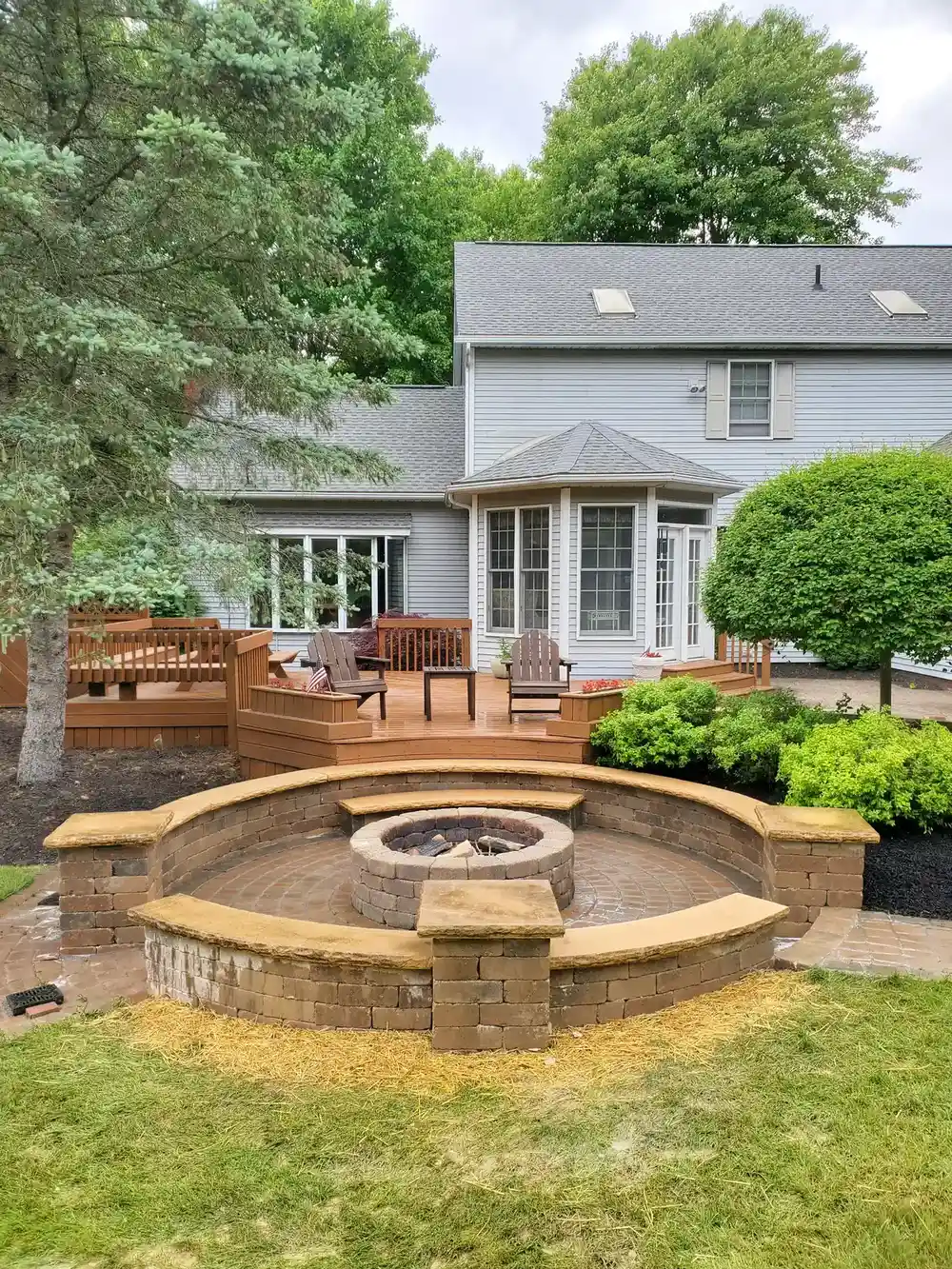 Circular paver fire pit, seat wall, deck, and layered backyard plantings