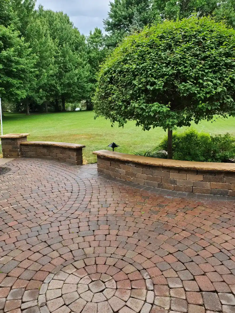 Curved paver patio and seat wall overlooking a lawn with mature trees