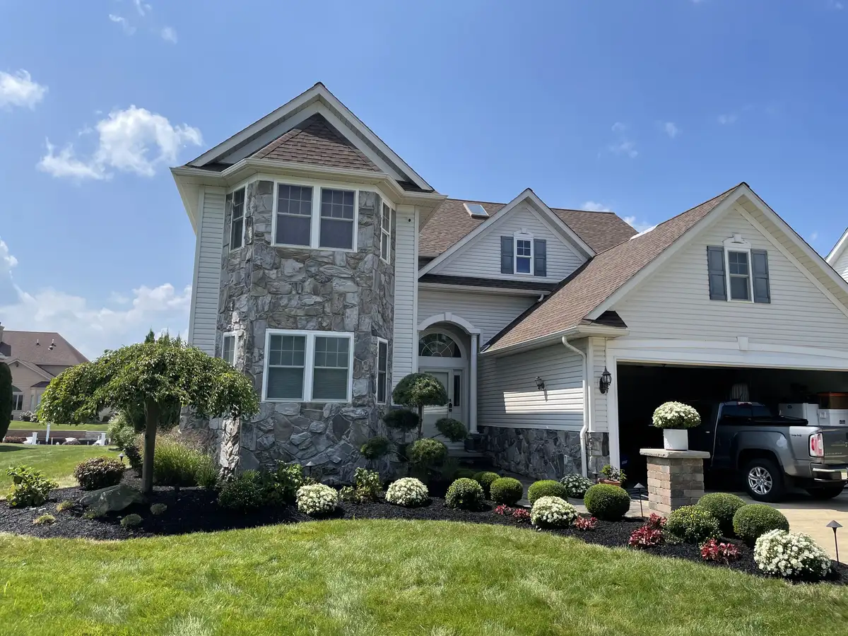 Two-story home with layered foundation plantings, ornamental trees, and fresh dark mulch