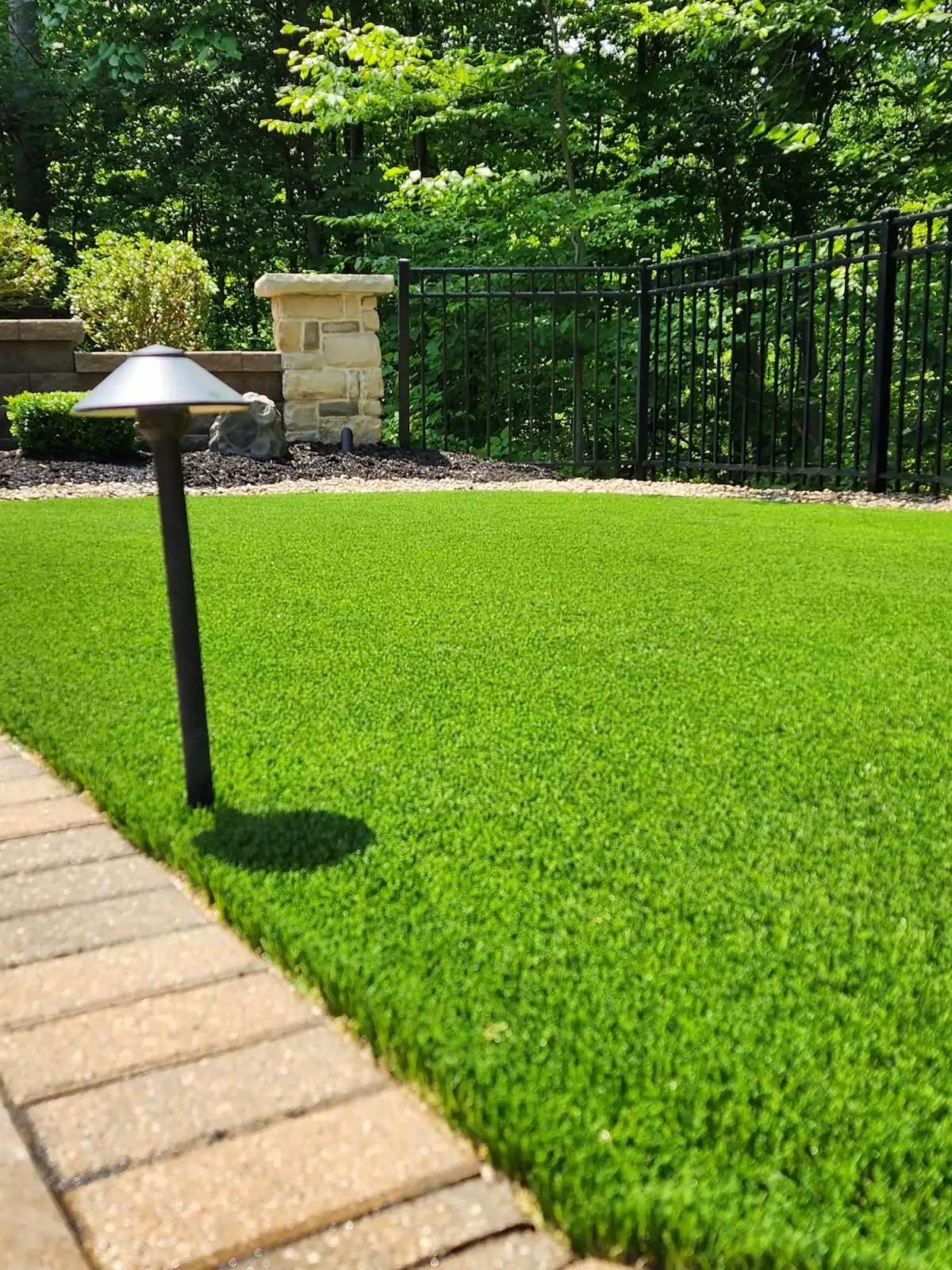 Lush synthetic turf lawn with landscape path light and iron fence in backyard